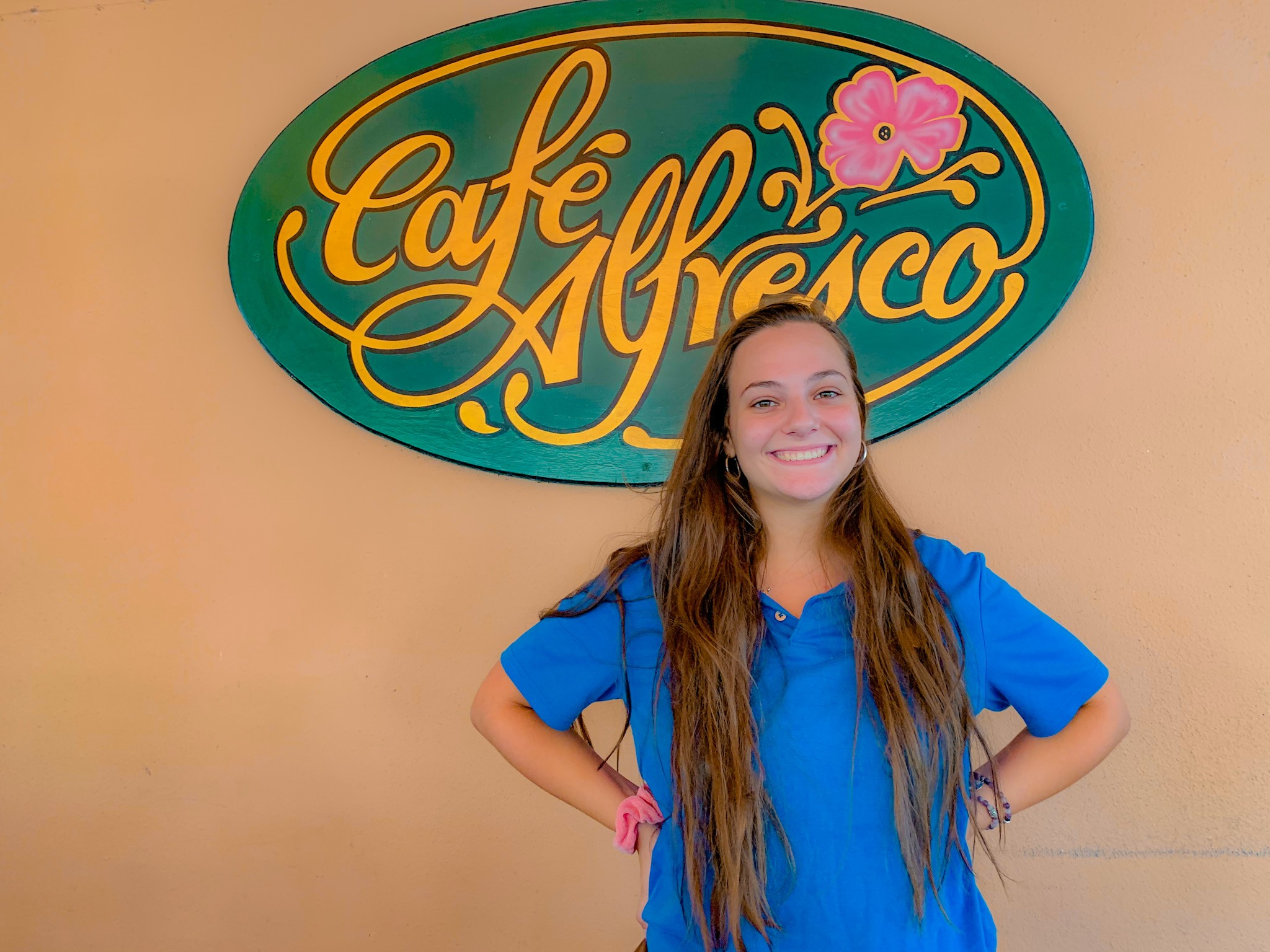 Emily, a server at Café Alfresco, standing in front of the restaurant's sign