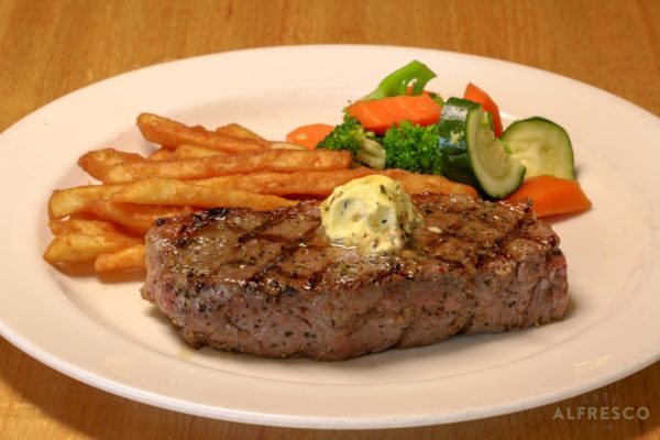 A plate with a New York strip steak with butter, a handful of fries and mixed vegetables