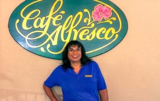 Dina stands in front of the Café Alfresco sign on the outdoor patio.